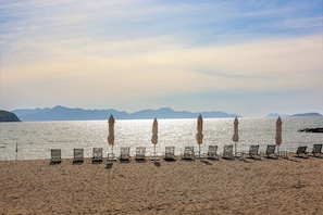 Een privéstrand, ligstoelen aan het strand, parasols, beachvolleybal