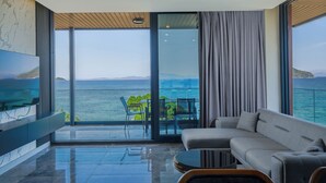 Un salon moderne doté d’un grand téléviseur à écran plat, d’un canapé, d’une table basse et offrant une vue sur la mer grâce à de grandes fenêtres du sol au plafond.