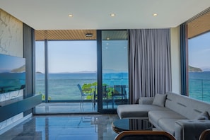 Un salon moderne doté d’un grand téléviseur à écran plat, d’un canapé, d’une table basse et offrant une vue sur la mer grâce à de grandes fenêtres du sol au plafond.