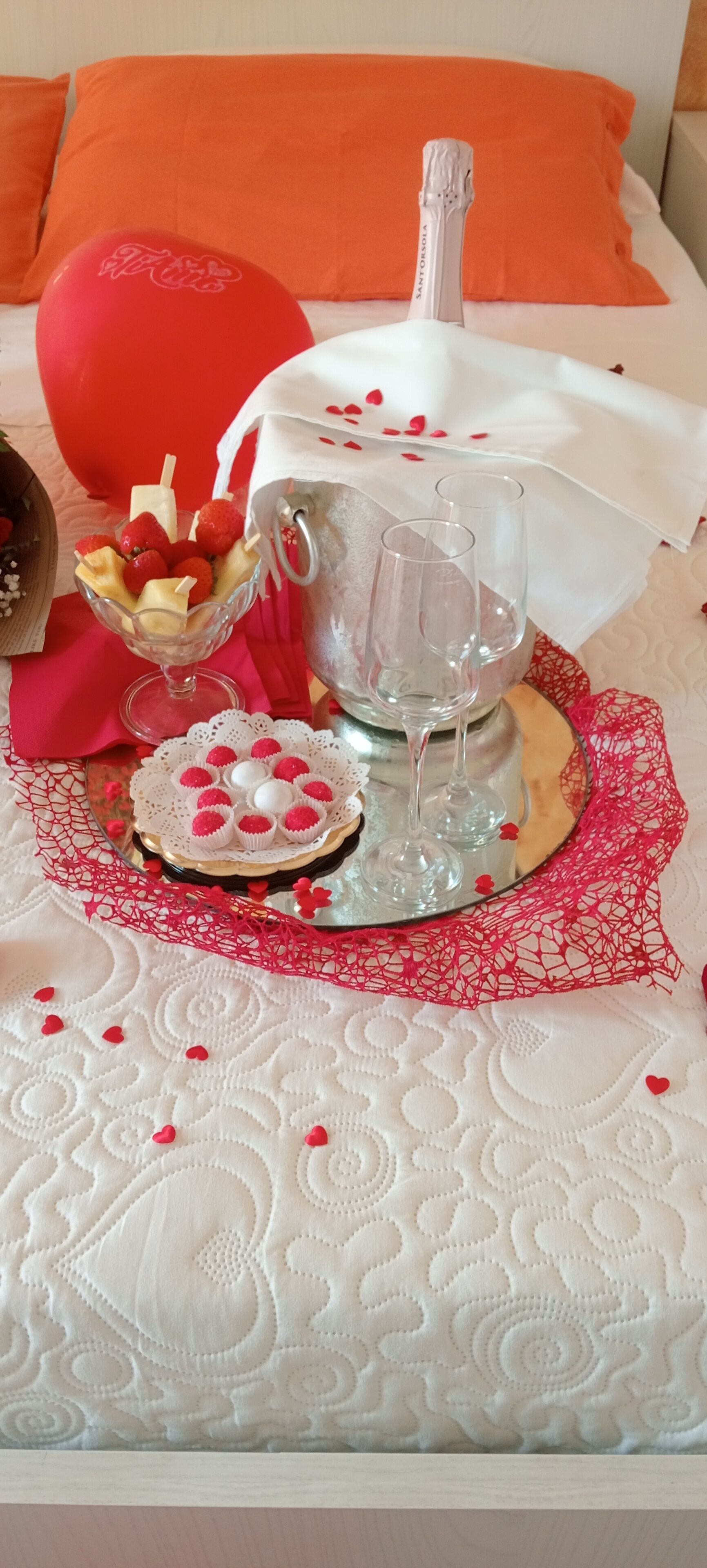 A bed with a white and orange color scheme, a clear glass pitcher, and a bowl of fruit on a lace doily.
