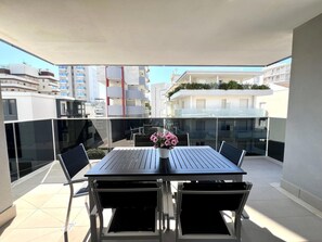 A balcony with a table and chairs, a potted plant, and a view of surrounding buildings. - Holiday apartment with air conditioning (Lignano)