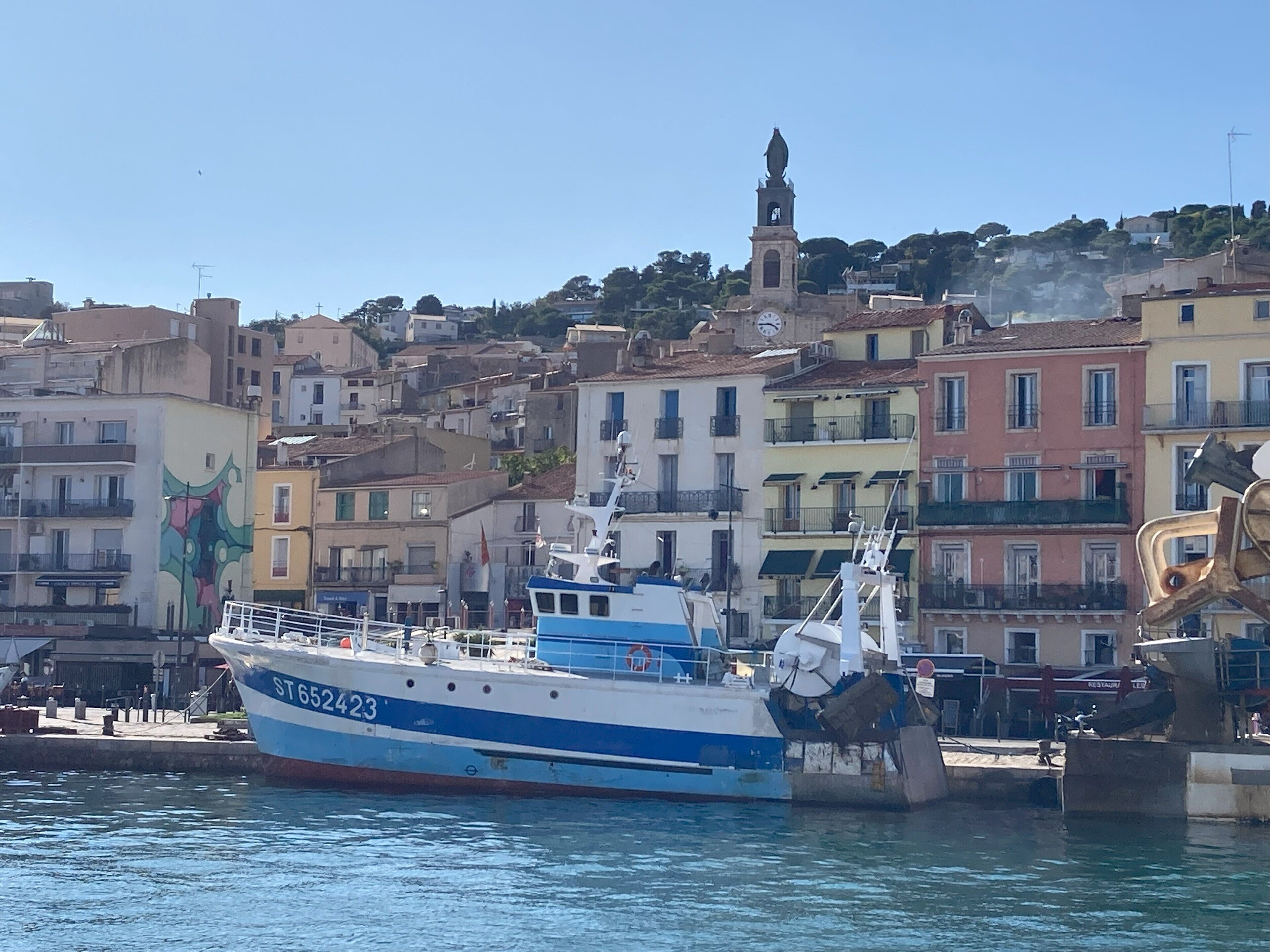 A boat docked at a harbor with a backdrop of colorful buildings and a bell tower.