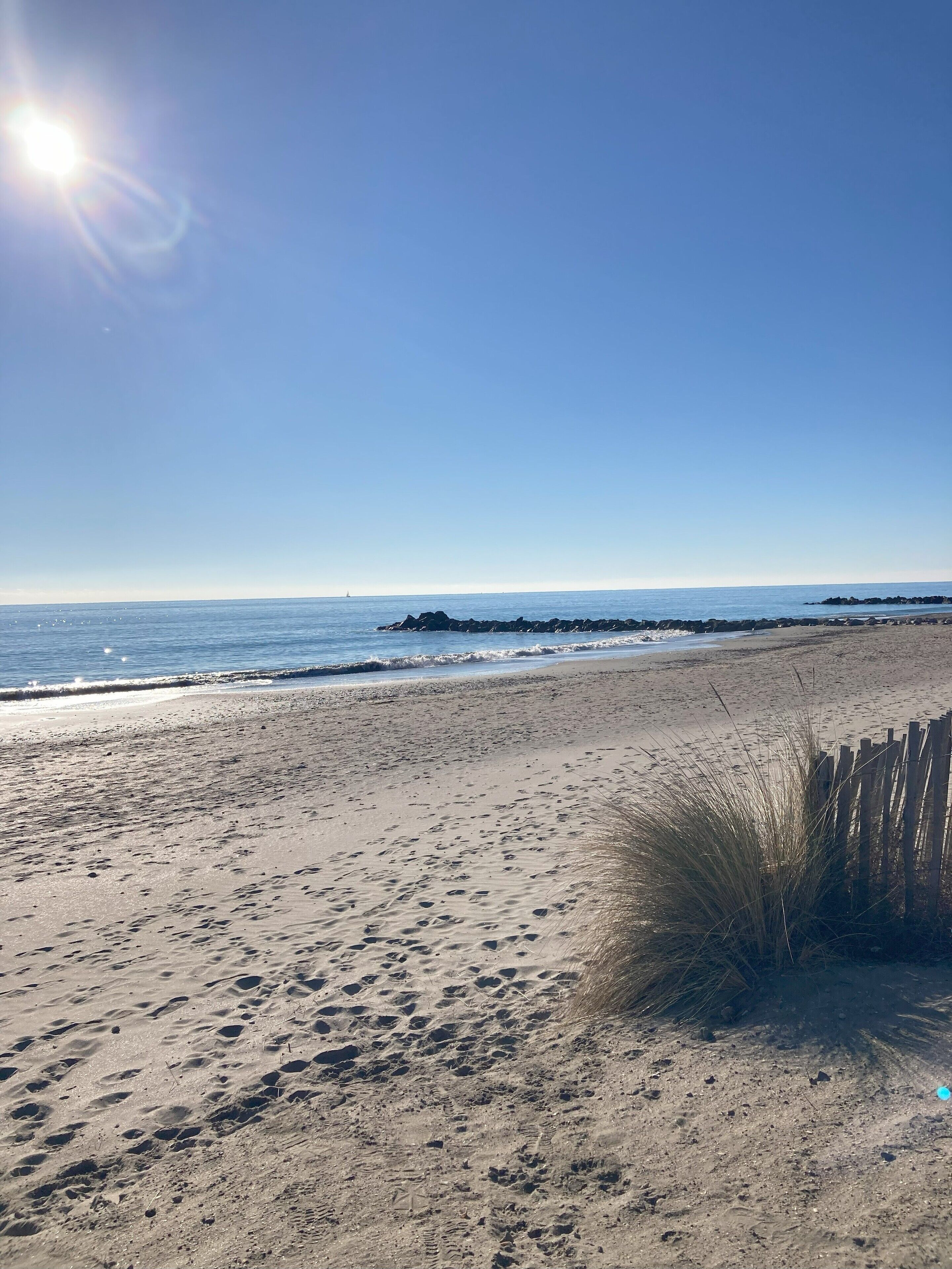A sandy beach with footprints, a wooden fence, and a clear sky.