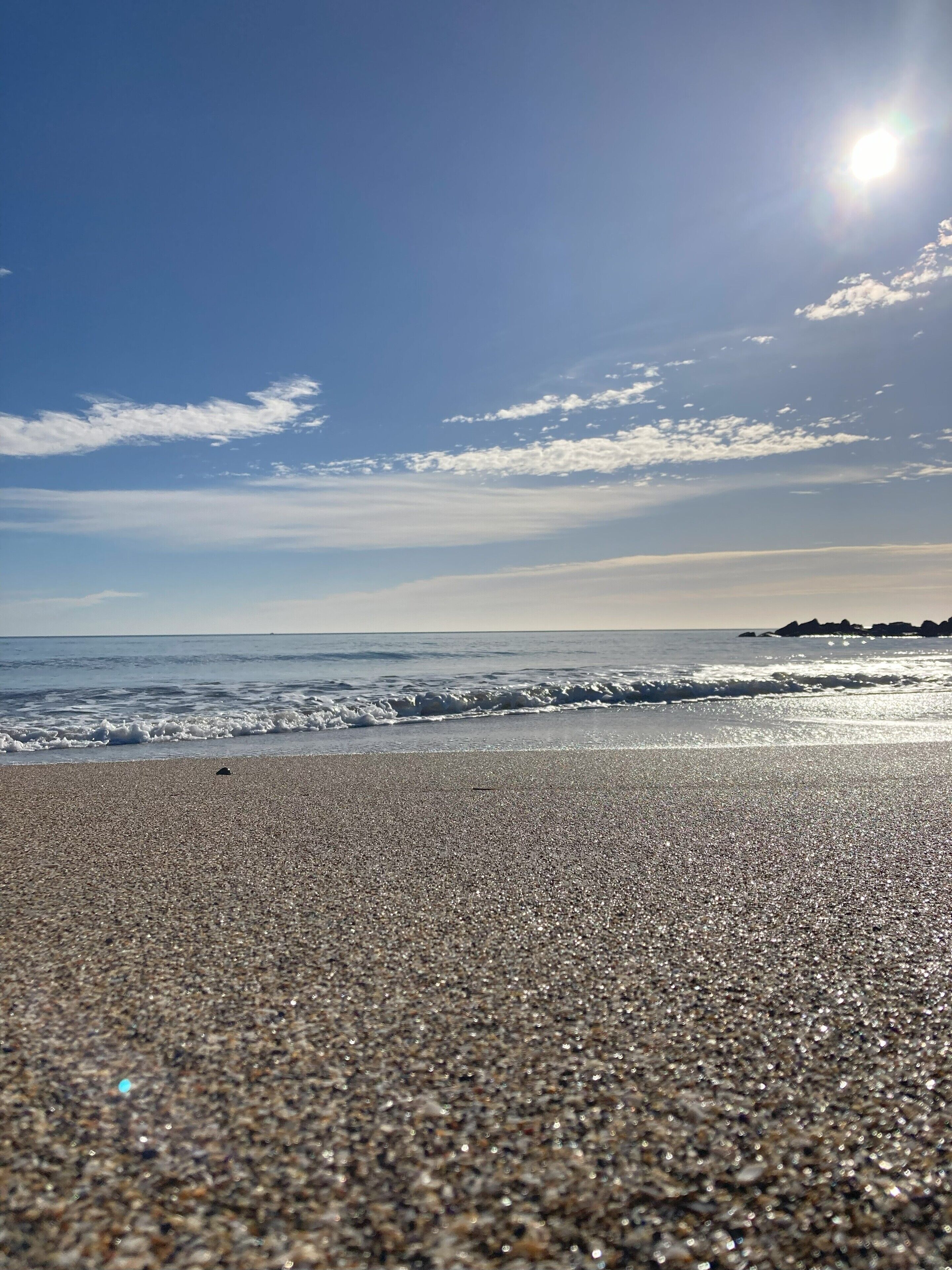Ein Strand mit Kieselsteinen und Wellen, ein klarer Himmel und die Sonne scheint.