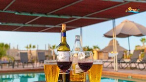 Escena junto a la piscina con una mesa que sostiene dos botellas de vino y dos copas, una botella de cerveza y una copa de cerveza.
