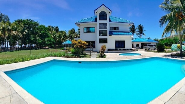 A resort with a large swimming pool, a multi-story building, and palm trees. - Villa del Nico


 (Pagudpud)