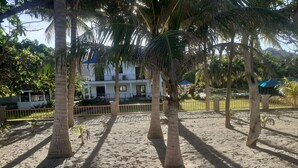 A sandy area with palm trees and a white building with a blue roof. - Villa del Nico


 (Pagudpud)