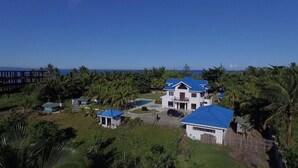 A large house with a blue roof, surrounded by palm trees and a view of the ocean. - Villa del Nico


 (Pagudpud)