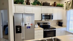 Una cocina con gabinetes blancos, un refrigerador de acero inoxidable, un microondas, un horno y un lavadero.