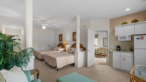 Habitación de hotel con dos camas, kitchenette, comedor y sala de estar con sofá verde y planta.