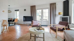 A living room with a TV, two armchairs, a small round table, and a dining area with chairs and a table.