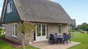 A house with a thatched roof, brick exterior, and a patio with a table and chairs.