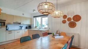 A modern kitchen with a wooden dining table, chairs, and pendant lights.