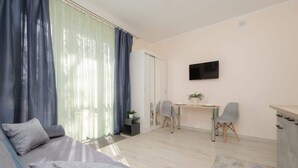 A modern living room with a sofa, a dining table with chairs, a TV mounted on the wall, and a kitchen area. - Comfortable Studio | Next to the Royal Baths (Warszawa)