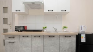 A modern kitchen with grey cabinets, a black refrigerator, a microwave, a kettle, and a small potted plant. - Comfortable Studio | Next to the Royal Baths (Warszawa)
