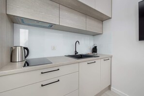 Une cuisine moderne avec des meubles de couleur claire, une bouilloire en acier inoxydable, un robinet noir et une hotte intégrée.