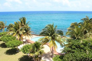 A tropical resort with a swimming pool surrounded by palm trees and a view of the ocean. - Seaside Condo 5 Penthouse @ Whispering Seas (Tower Isle)