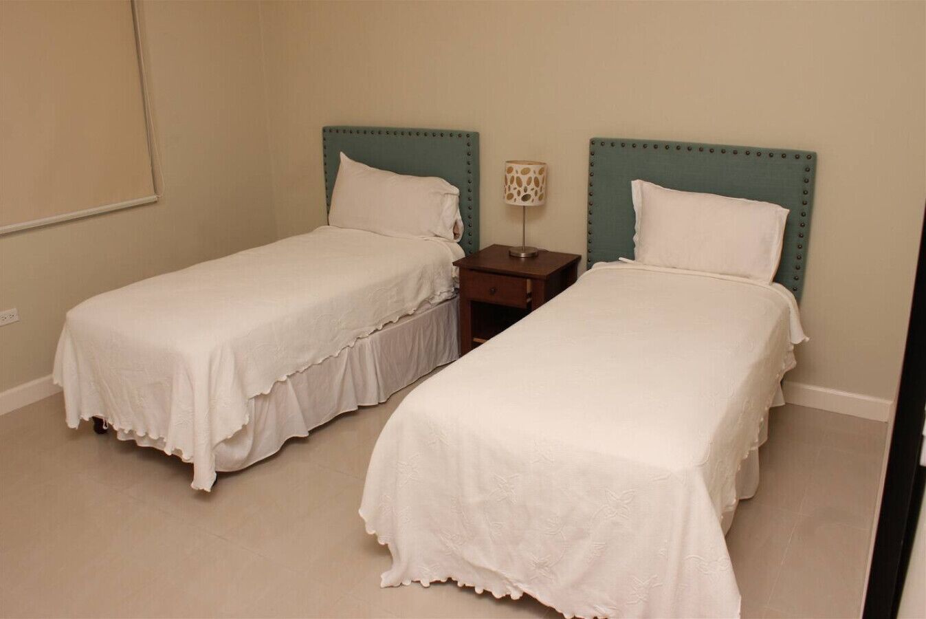 Deux lits simples avec des têtes de lit assorties, une table de chevet avec une lampe et un mur sobre.