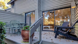 Une terrasse en bois avec des meubles d’extérieur, une plante en pot et une porte-fenêtre coulissante donnant sur un espace intérieur.
