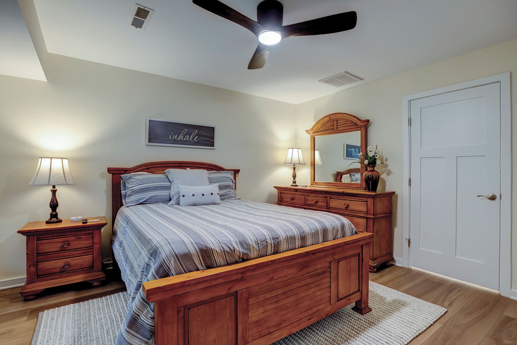 A bedroom with a wooden bed, nightstands, a ceiling fan, a mirror, and a door.