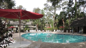 Une piscine entourée d’arbres et dotée d’une terrasse en briques, avec des chaises longues et des parasols.