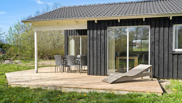 Una casa moderna de madera con un porche cubierto, mobiliario exterior y un amplio ventanal.