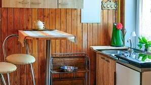 A kitchen with wooden walls, a small table with a teapot, a green kettle, and a sink.