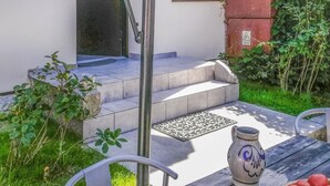 A patio with a stone bench, a metal chair, a decorative vase, and a fruit basket.