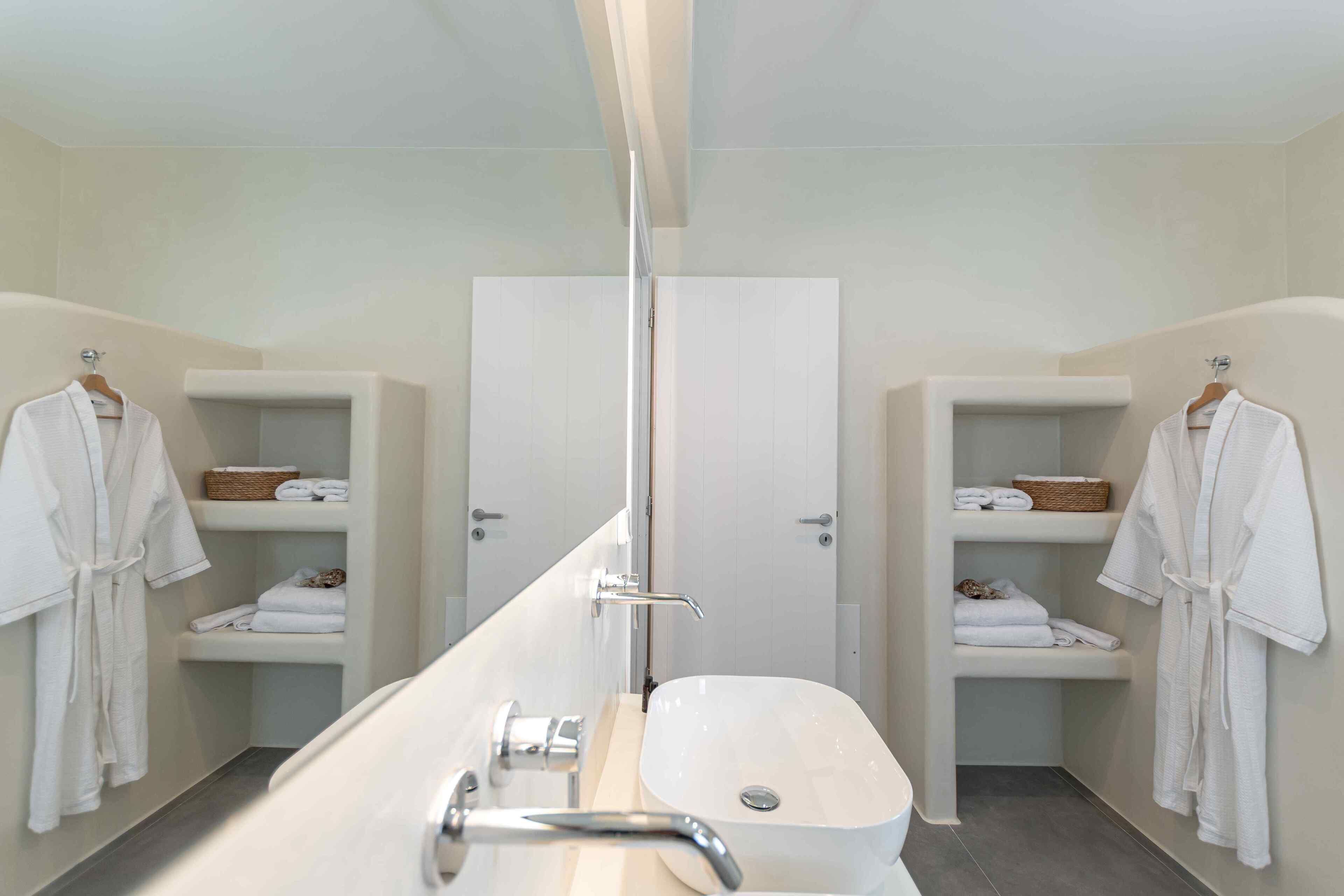 A modern bathroom with a long vanity, two towel racks, and shelves with folded towels and a basket.