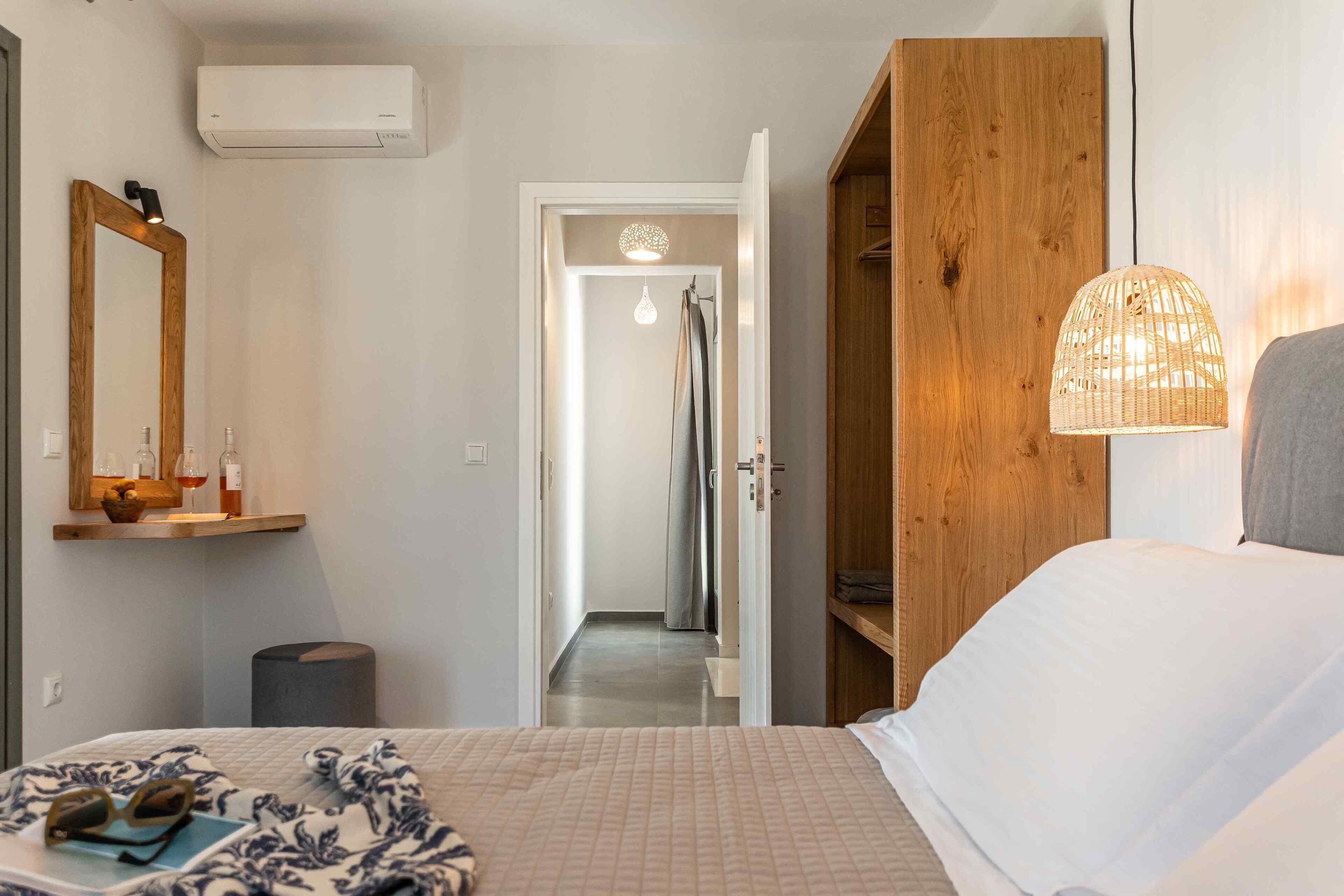 A hotel room with a bed, a wooden wardrobe, a mirror, a hanging light fixture, and a shower area.