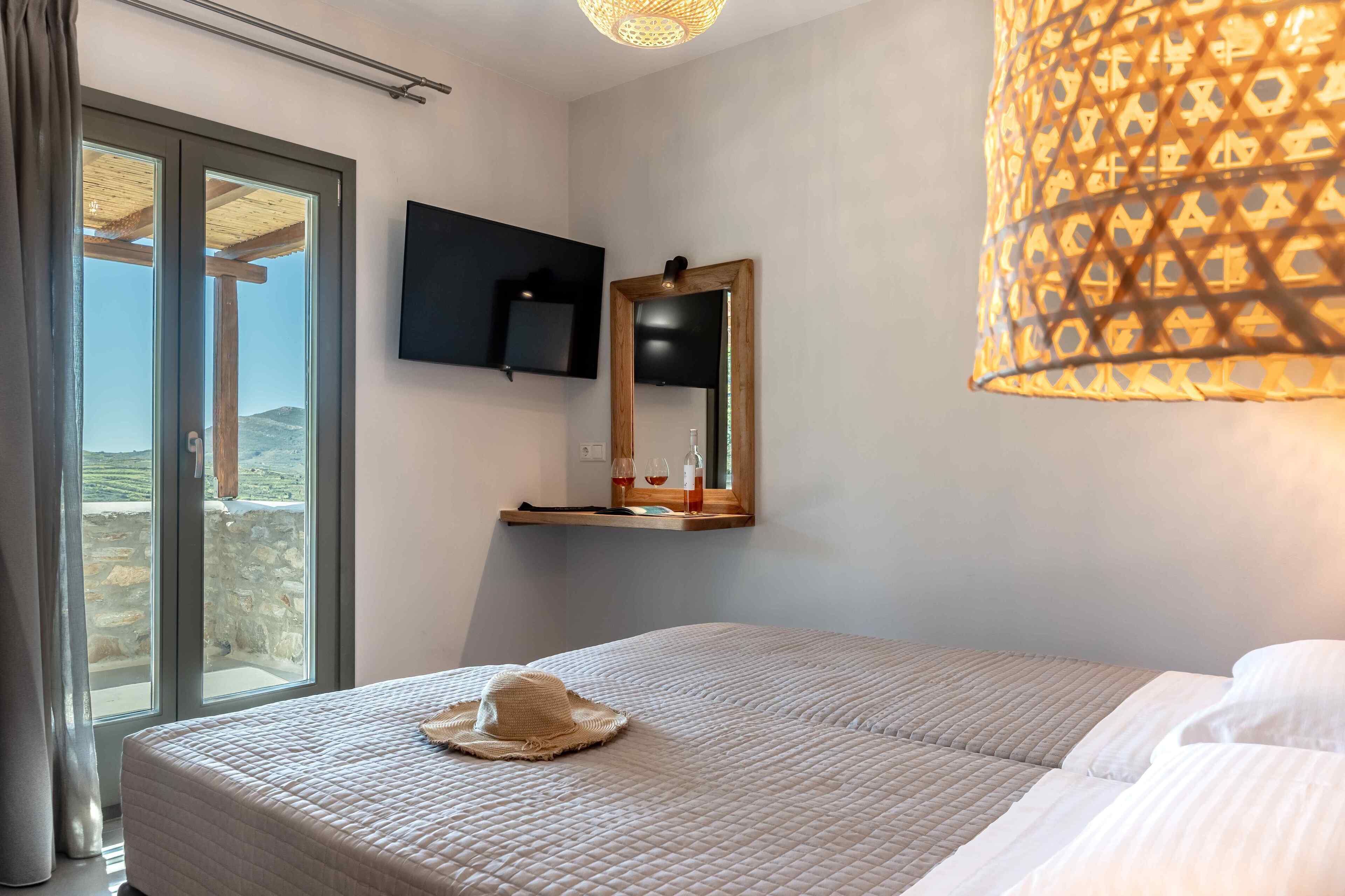 Un dormitorio con una cama grande, un televisor montado en la pared, un espejo sobre la cama y una ventana con vistas al exterior.
