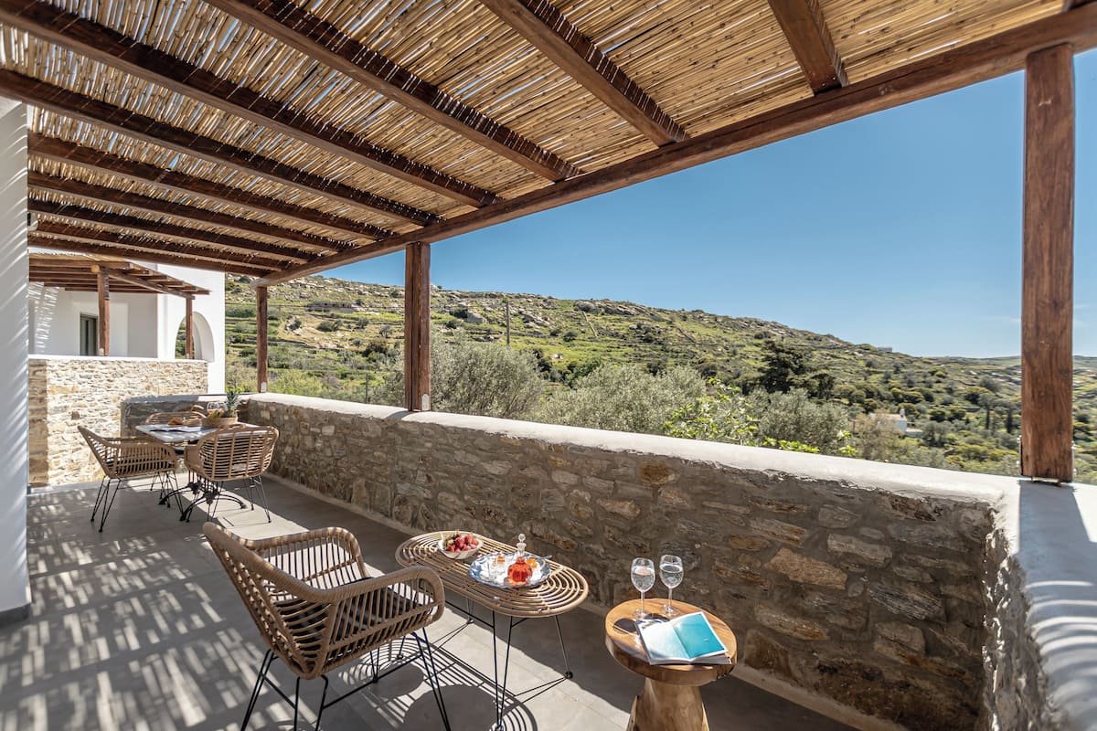 Um terraço com mobiliário de vime, uma parede de pedra e vista para colinas ondulantes.