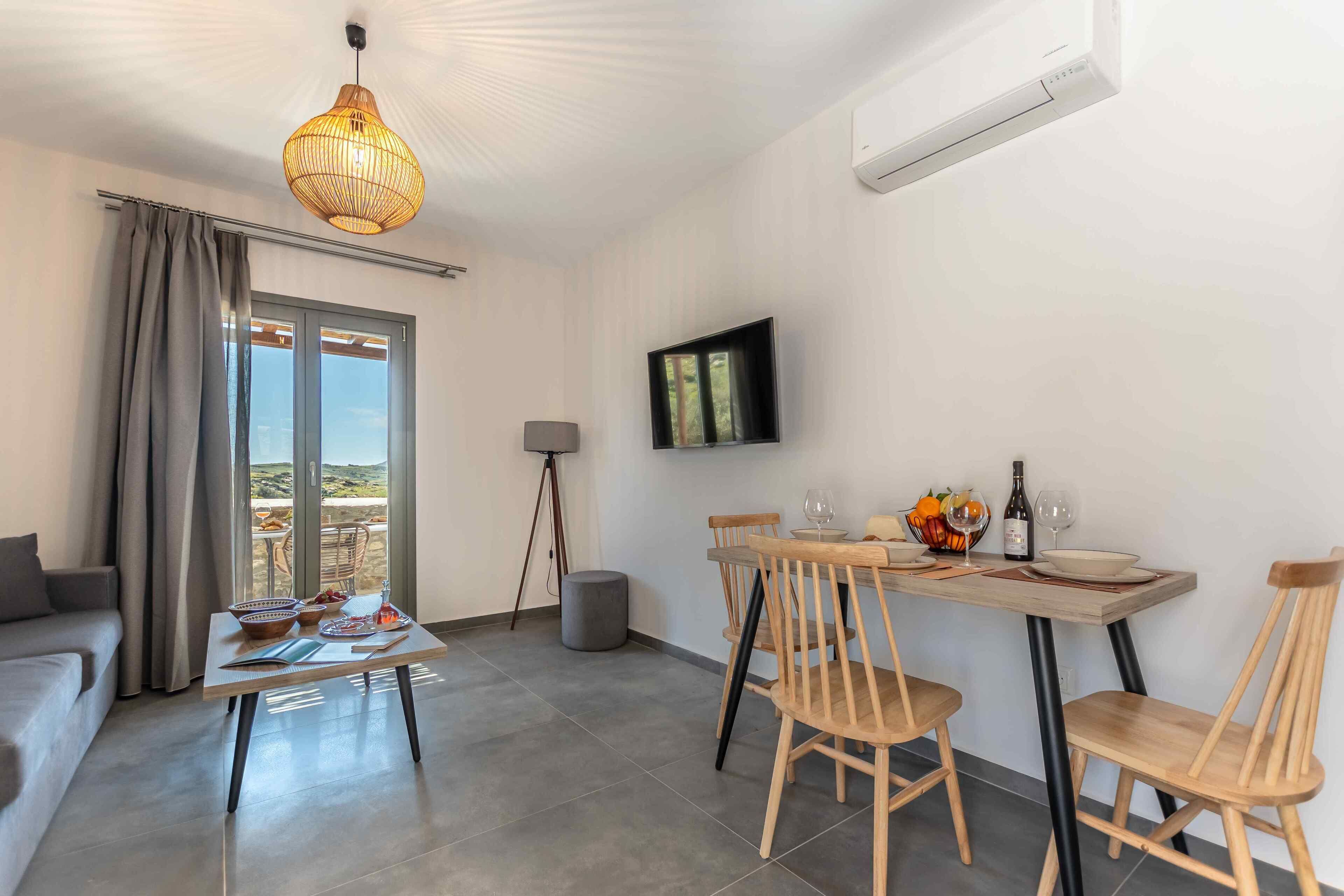 Ein modernes Wohnzimmer mit einer Couch, einem Esstisch mit Stühlen, einem an der Wand befestigten Fernseher und einem Balkon mit Vorhängen.