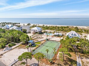 Enjoy a serene beachfront setting with a tennis court and pool surrounded by lush greenery.