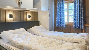 A double bed with white bedding in a room with wooden paneling and a window with blue curtains.