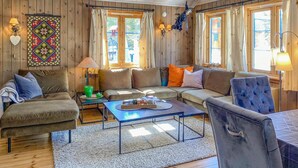 A cozy living room with wooden walls, a sofa set, a coffee table, and a decorative wall hanging.