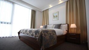 Une chambre d’hôtel avec un grand lit, deux tables de chevet, une petite table et un tableau encadré au mur.