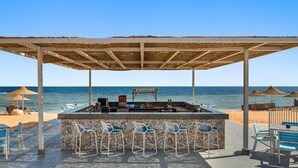 Un bar situé en bord de mer, doté d’un comptoir en pierre, de tabourets et de parasols.