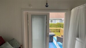 Una habitación con puerta corrediza de vidrio que da a un área exterior con piscina y terraza de madera.