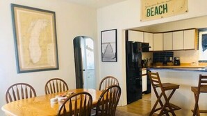 Un comedor con una mesa y sillas de madera, un refrigerador y una cocina con alacenas y una encimera.