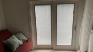 Una habitación con un sofá rojo, dos puertas blancas con persianas y una cortina blanca.