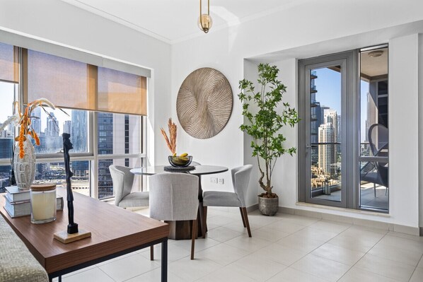 Un salon moderne comprenant un coin repas, de grandes fenêtres offrant une vue sur la ville, une table ronde et une plante en pot.