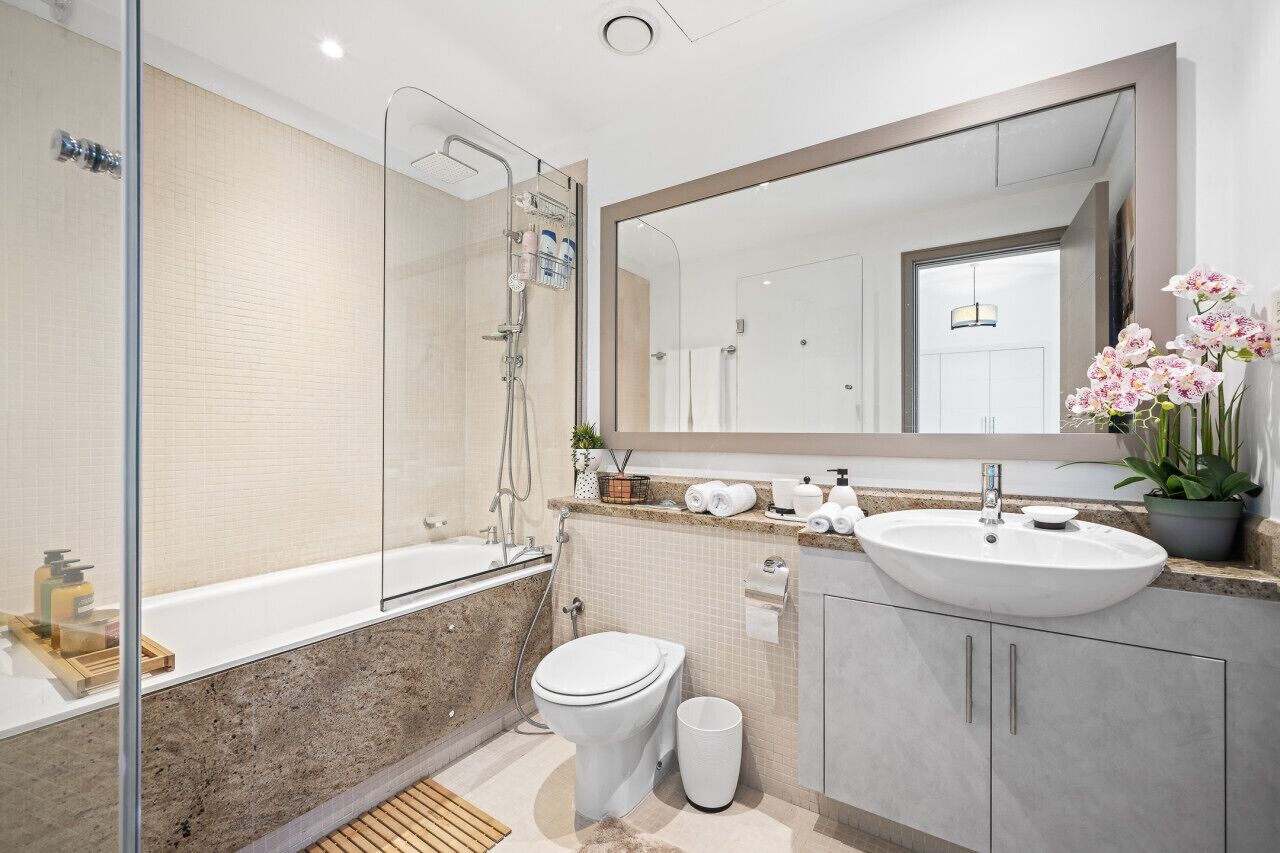 Une salle de bain moderne dotée d’une douche à parois de verre, d’une baignoire sur pieds, de toilettes et d’un lavabo avec un grand miroir au-dessus.