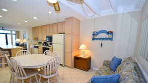 A compact kitchen with a dining table and chairs, a refrigerator, and a small island with a lamp. - Jada 1F-Oceanside 77th St, Free WiFi, Pool, Elev, W/D, AC (Ocean City)