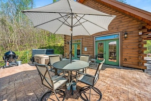 An outdoor patio with a round table and chairs, a grill, and a large umbrella.