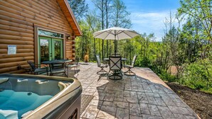 Una cabaña de madera con un patio que incluye un jacuzzi, asientos al aire libre y vistas del bosque circundante.