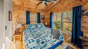 Un dormitorio de cabaña de madera con cama, ventilador de techo y ventana con cortinas.