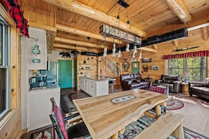 L’intérieur chaleureux d’un chalet avec une table à manger en bois, des canapés en cuir, un coin cuisine et un escalier menant à un autre niveau.