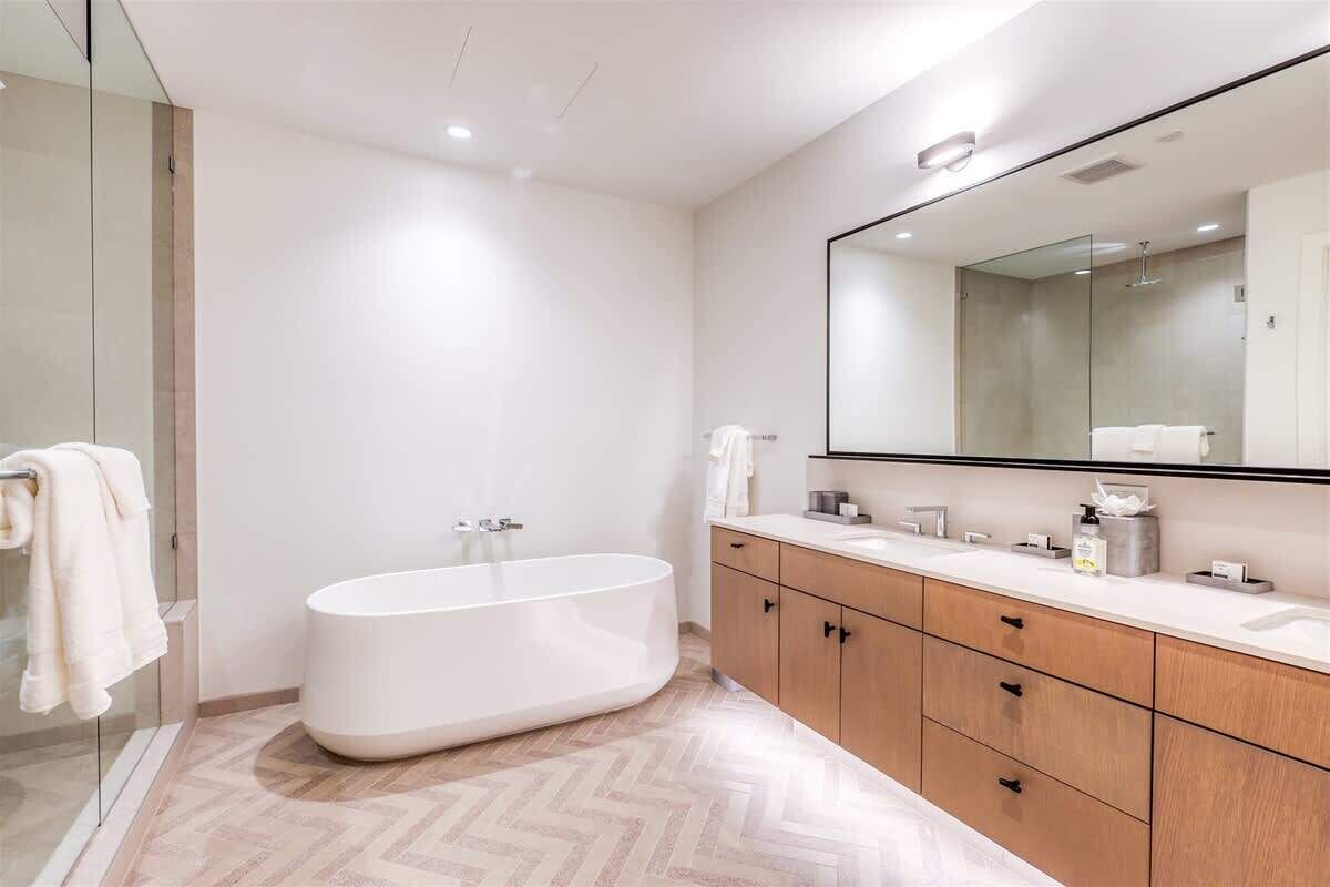 A modern bathroom with a freestanding bathtub, a large mirror, and a wooden vanity with drawers.