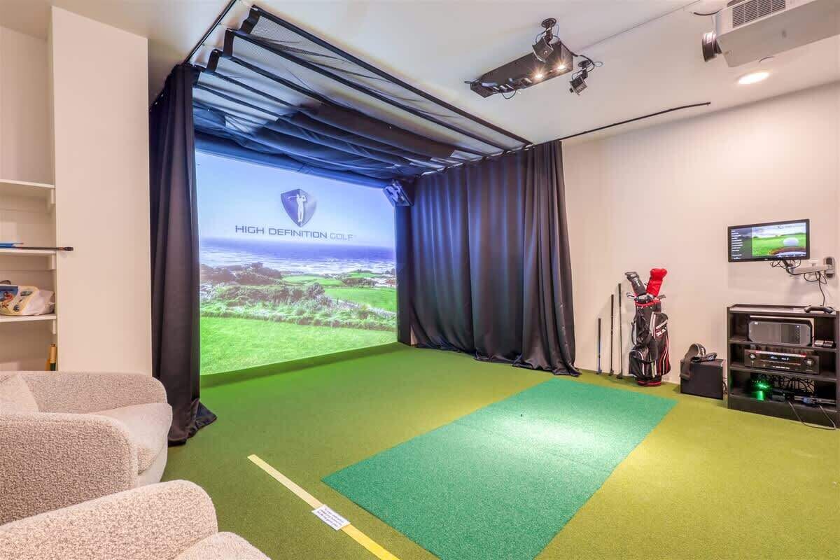 Una habitación con una pantalla grande mostrando 'HIGH DEFINITION GOLF', un bolso de golf y un proyector.